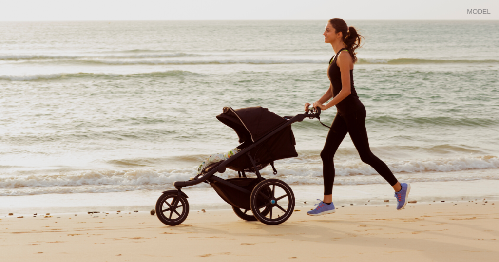 Woman pushing a stroller while running on the beach (model)